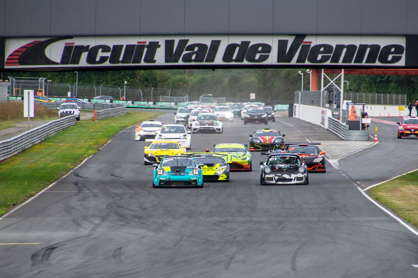 Départ groupé de voitures de course sous la ligne d'arrivée du Circuit du Val de Vienne